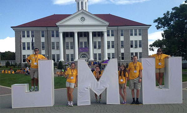 Ashleigh Cotting and other JMU students pose with people-sized letters: JMU, on The Quad during freshman orientation week.